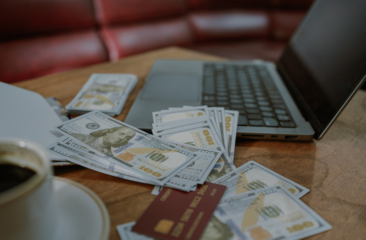 One hundred US dollar bills and laptop on workspace table.