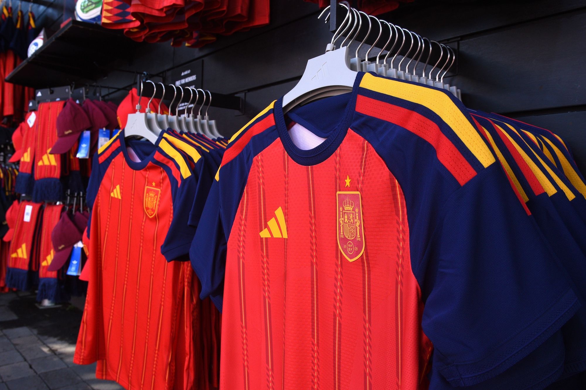 Rows of red and blue soccer jerseys with the Spanish national team crest and Adidas logo displayed on a store rack.