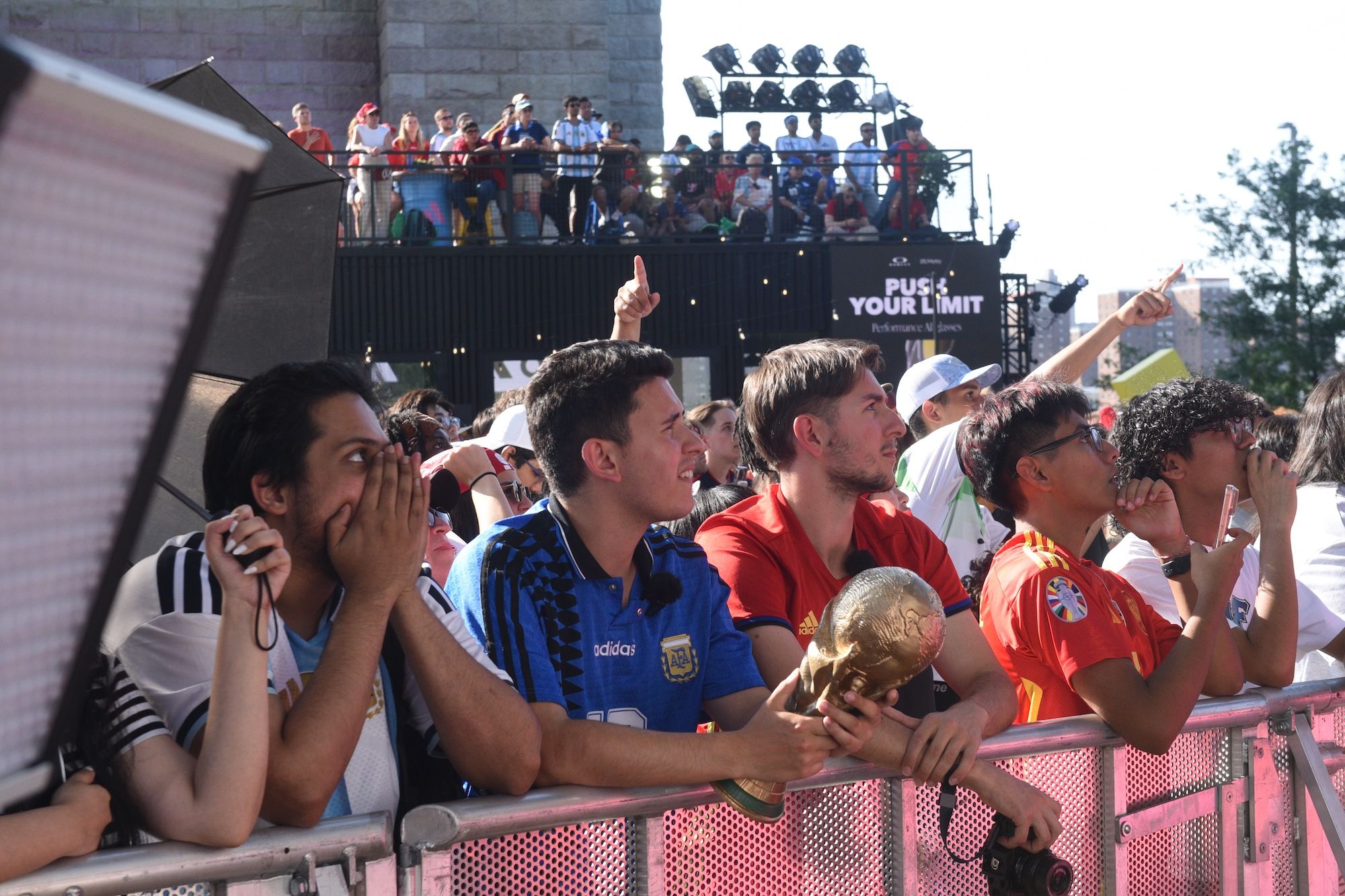 A large crowd of people watching an event, some wearing sports jerseys and holding a trophy.