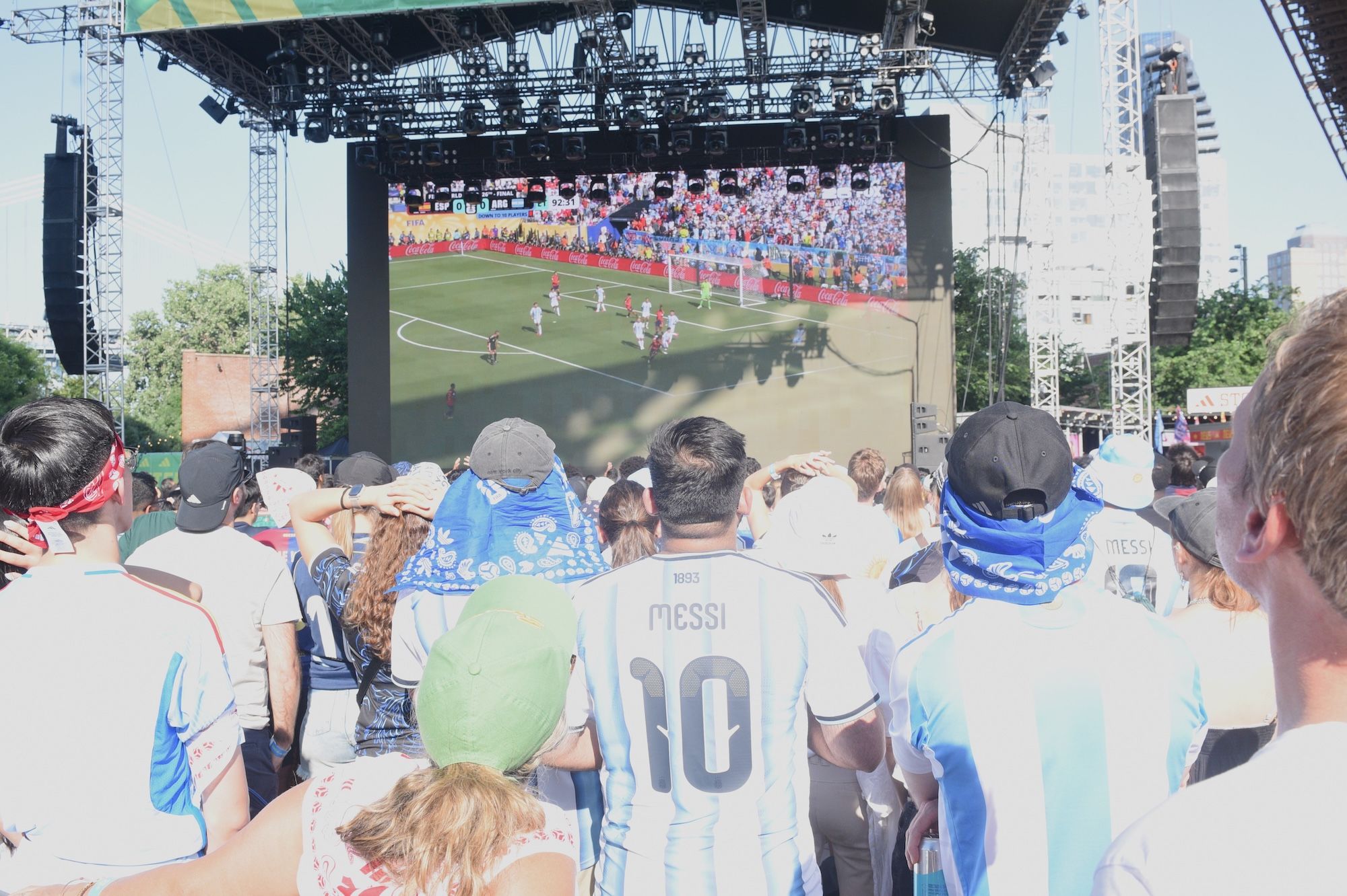 Large outdoor screen showing a soccer match, with a crowd of fans wearing jerseys with the number 10 and the name "Messi" on the back.