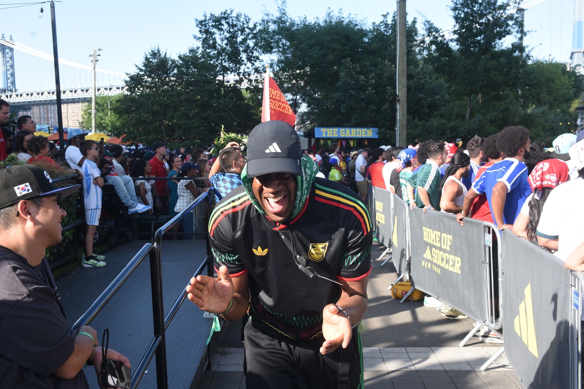Crowd of people at a sporting event, with a person in the foreground wearing a black jersey with the Adidas logo and "KING OF SOCCER" text.