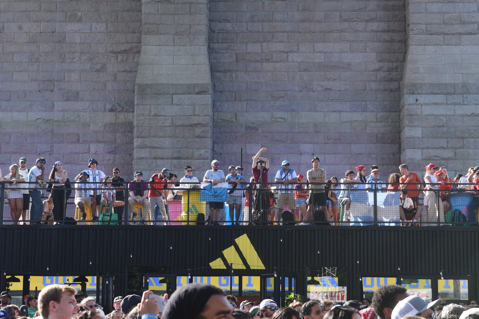Crowd of people gathered at a sporting event, with an Adidas logo visible on the barrier in the foreground.