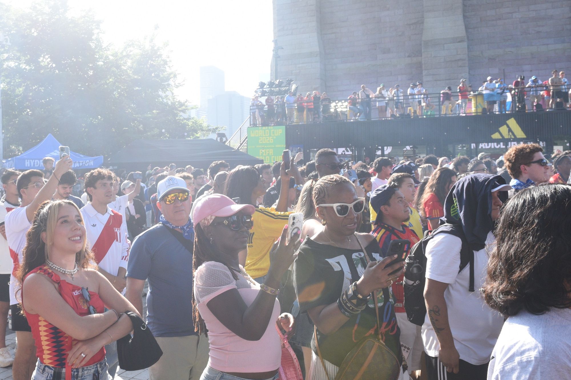 Crowded outdoor event with people holding signs and wearing colorful clothing. Adidas logo visible on some clothing.