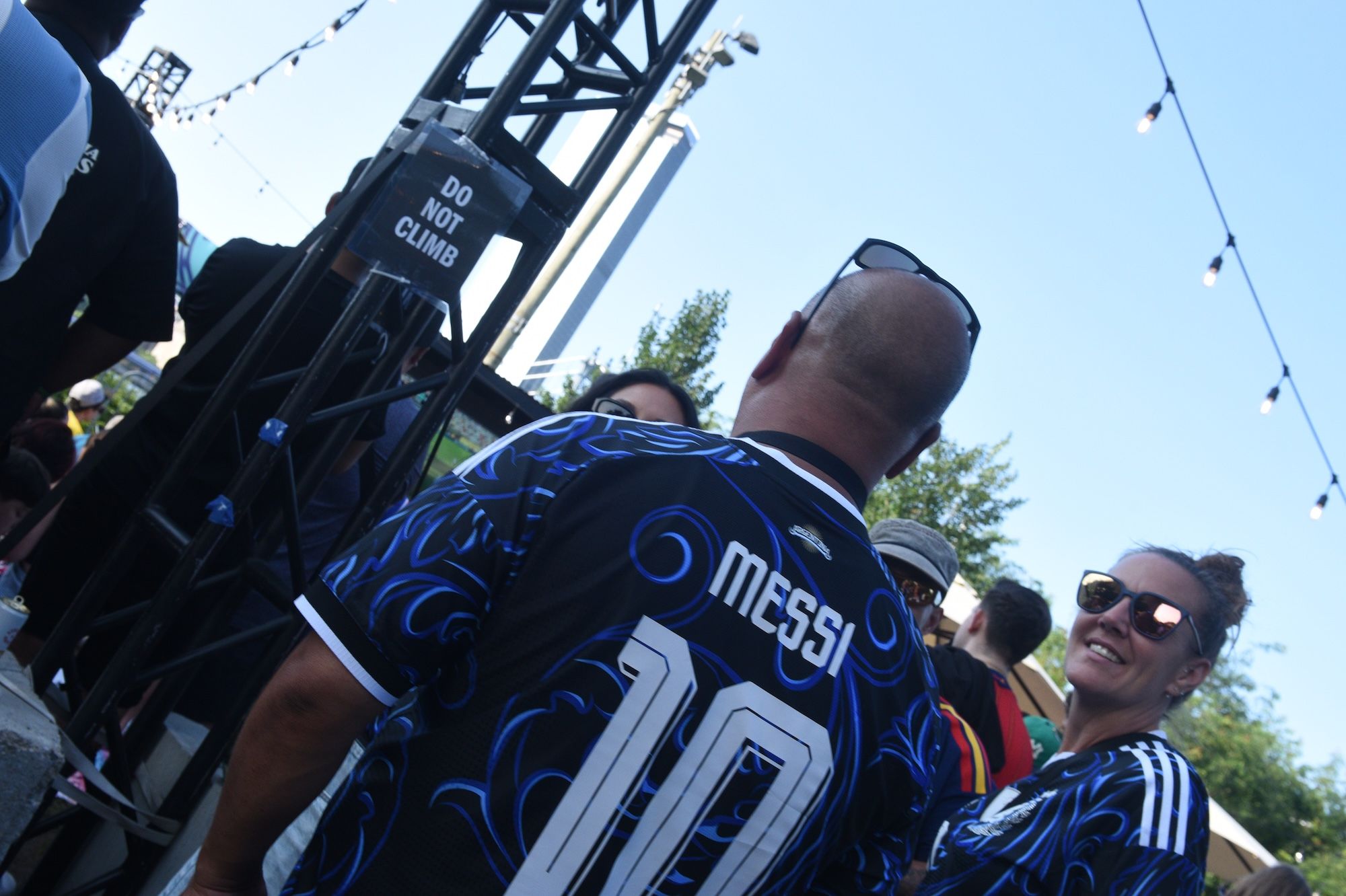 A person wearing a jersey with the number 10 and the Messi logo, standing in front of a "Do Not Climb" sign on a metal structure.