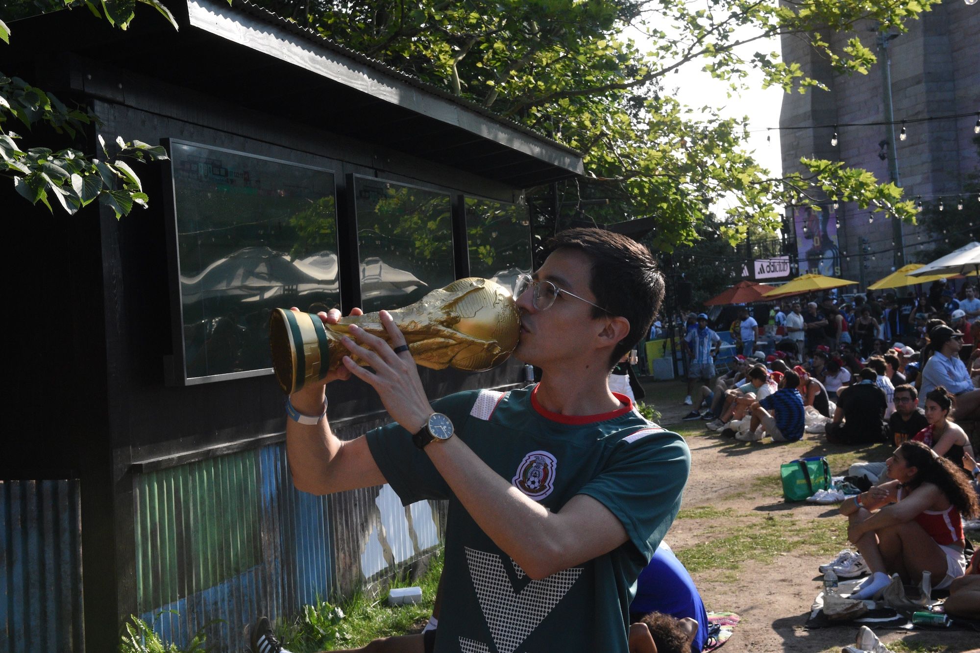 A person in a green jersey drinking from a large cup while surrounded by a crowd at an outdoor event.