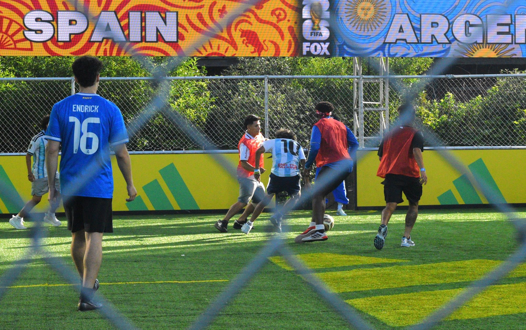 Several people playing soccer on a field with a "Spain" and "Argentina" backdrop and FIFA FOX branding.