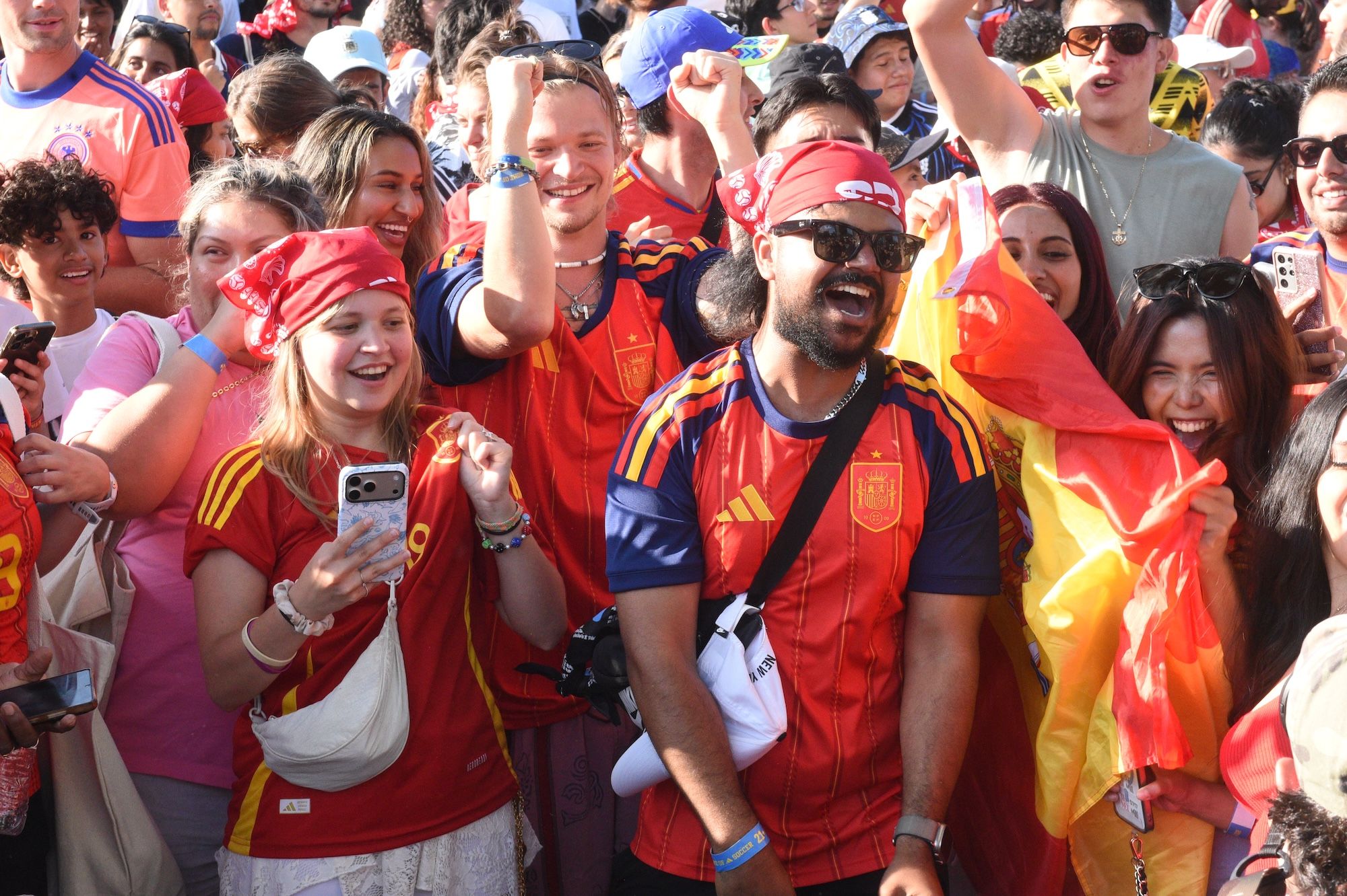 Crowd of enthusiastic fans wearing Spain national team jerseys and waving flags, cheering and celebrating together.