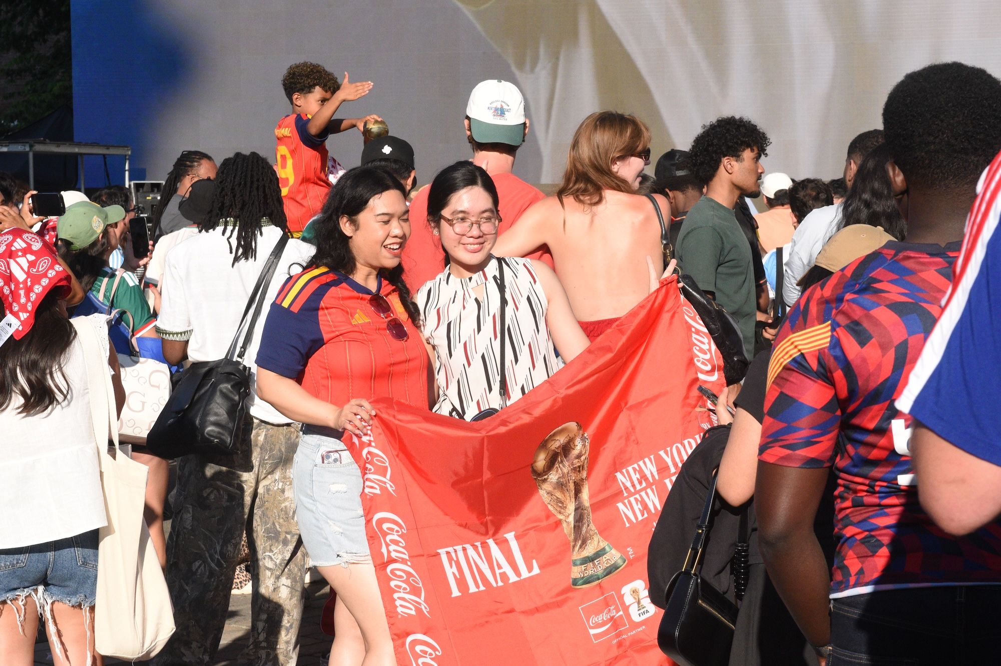 Crowd of people celebrating at a sporting event, holding up a large red Coca-Cola banner that says "FINAL".