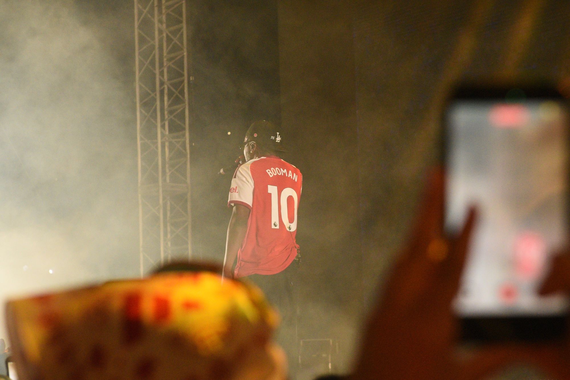 A red jersey with the name "Booman 10" is displayed in a dimly lit setting, with a blurred object in the foreground.