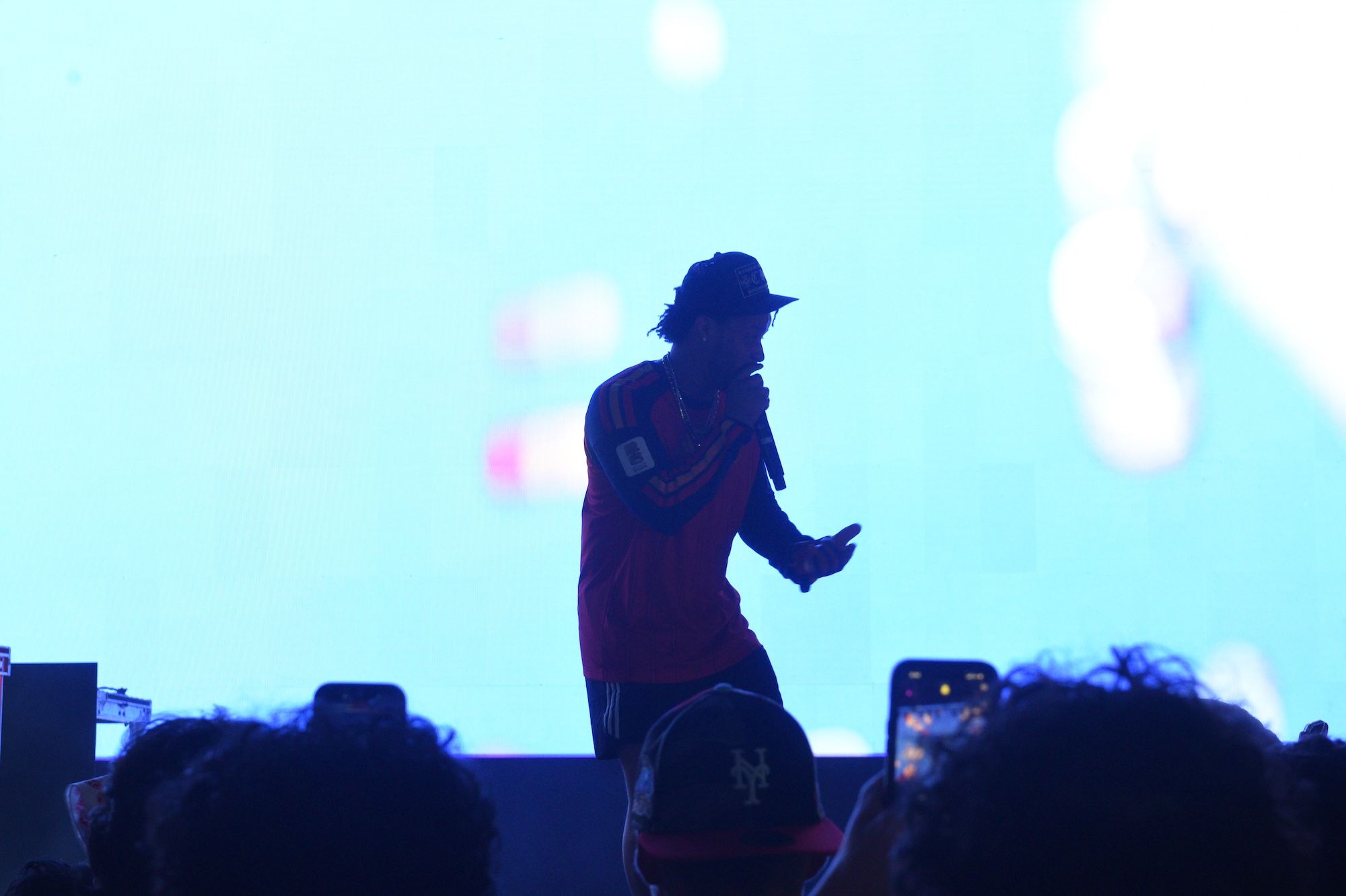 Silhouetted figure in a red jacket and hat performing on a stage against a bright, blurred background.
