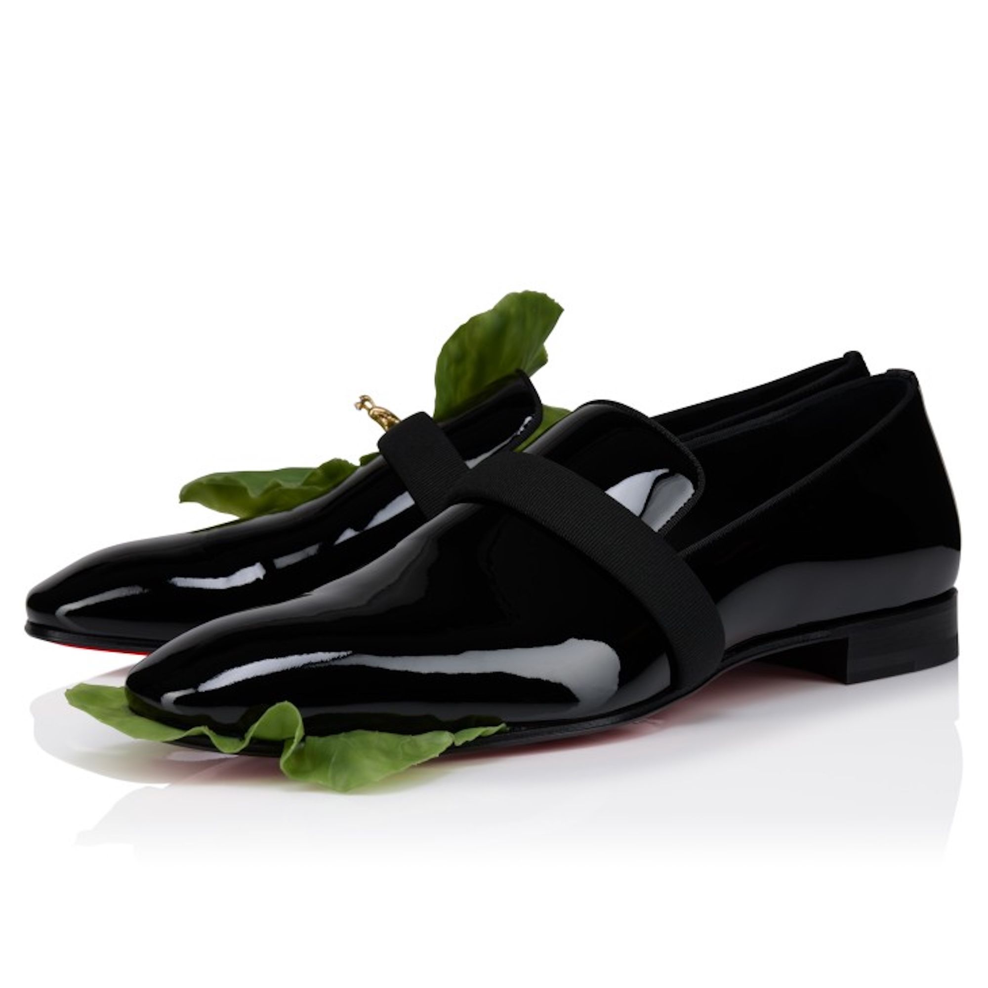 Black patent leather dress shoes with green leaves on a white background.