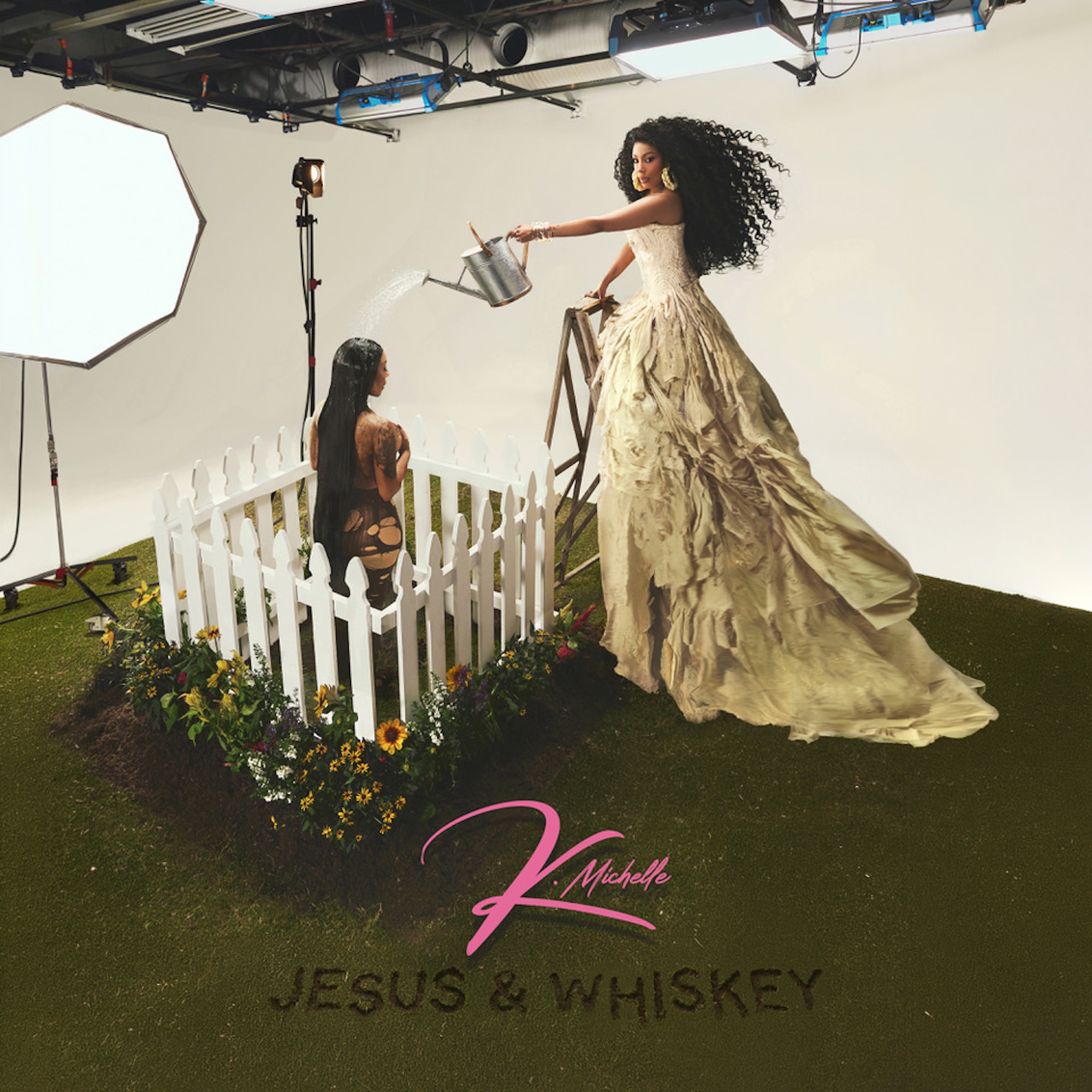 A woman in a flowing white dress stands in a studio setting, watering a potted plant. The backdrop features the text "Jesus & Whiskey" and the name "K. Michelle".