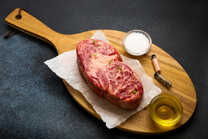 Fresh steak on a wooden cutting board with seasonings and oil