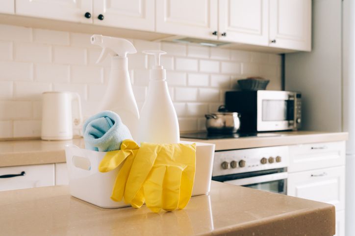 Kitchen cleaning supplies on countertop with gloves and spray bottles in modern white interior